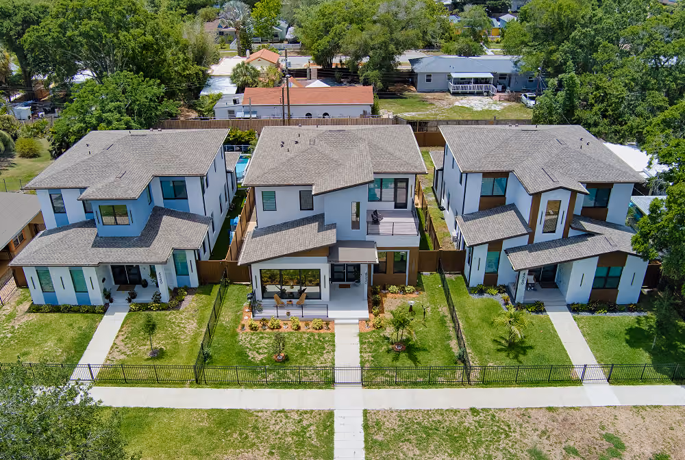 Aerial view of three modern two-story houses with front lawns and fenced yards in a residential area.