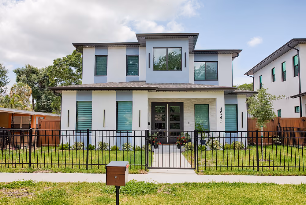 Modern two-story house with white exterior, green windows, black metal fence, and front yard lawn.