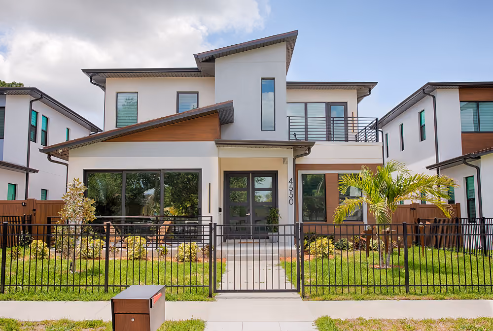 Modern two-story house with white walls, large windows, balcony, and black metal fence with gate.