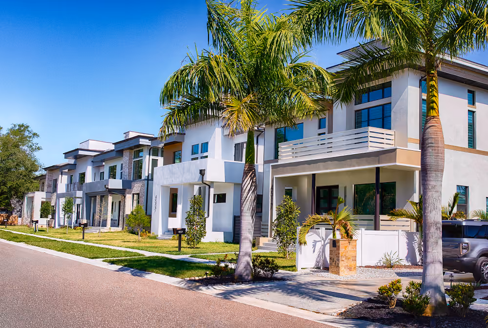 Row of modern two-story houses with palm trees and clear blue sky in a sunny neighborhood.