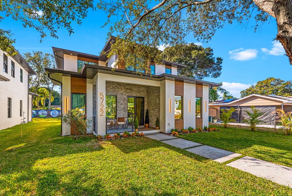 Modern two-story house with white and wood paneling, front porch, and well-maintained lawn under blue sky.