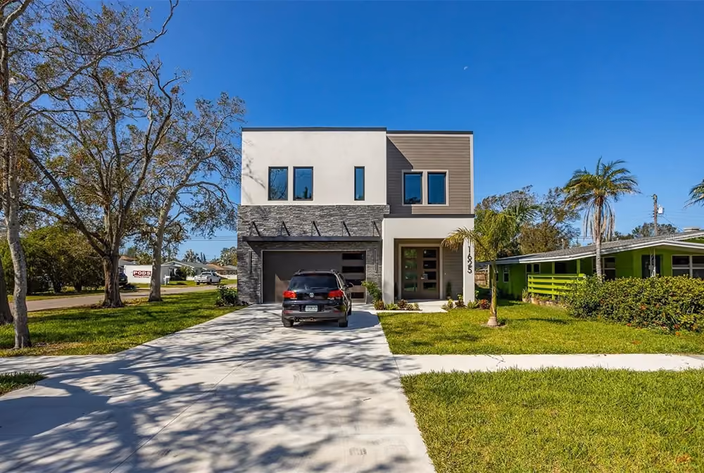 Modern two-story house with a black car on the driveway, green lawn, and clear blue sky.