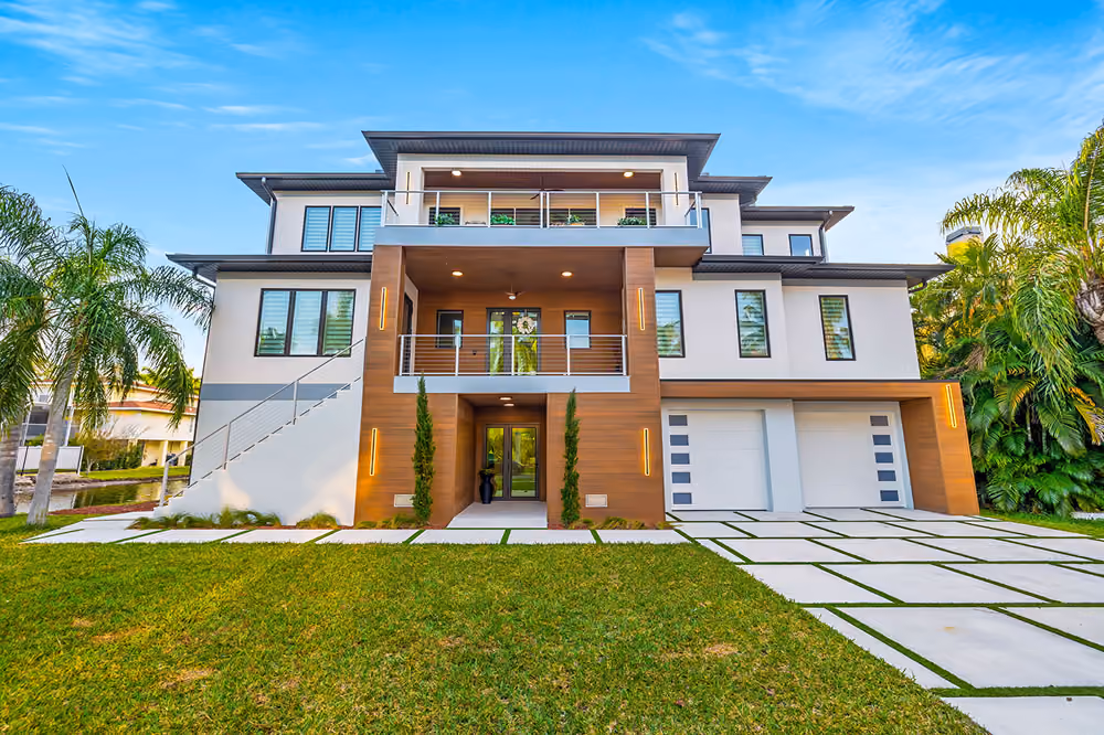 Modern three-story house with wood accents, large windows, balcony, garage, and green lawn with palm trees.