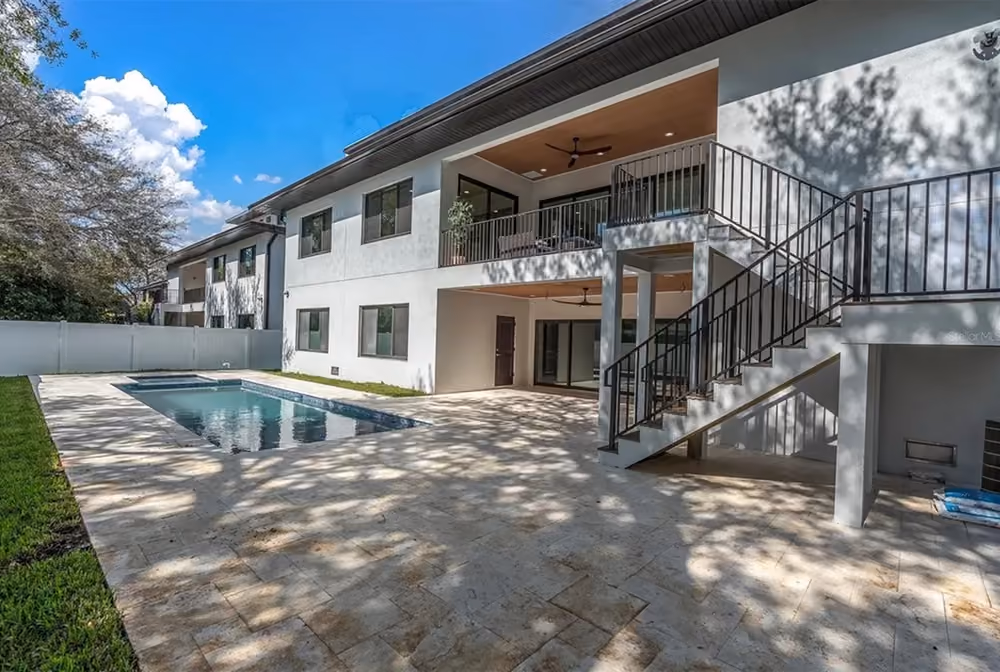 Backyard of a two-story house with a small rectangular swimming pool, patio, and stairs to a second-floor balcony.