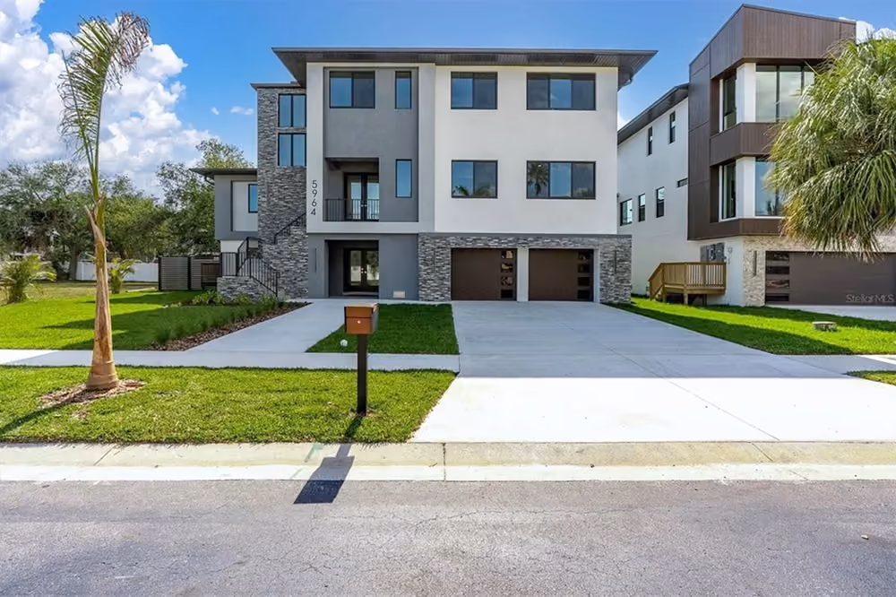 Modern two-story house with stone and white exterior, two garages, palm trees, and a mailbox.