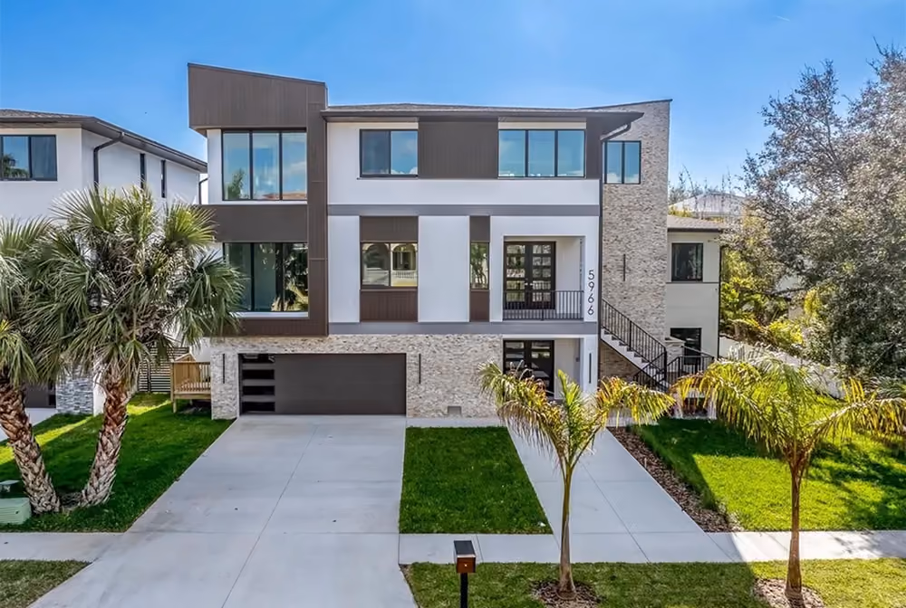 Modern two-story house with large windows, stone and white facade, two palm trees, and a driveway.