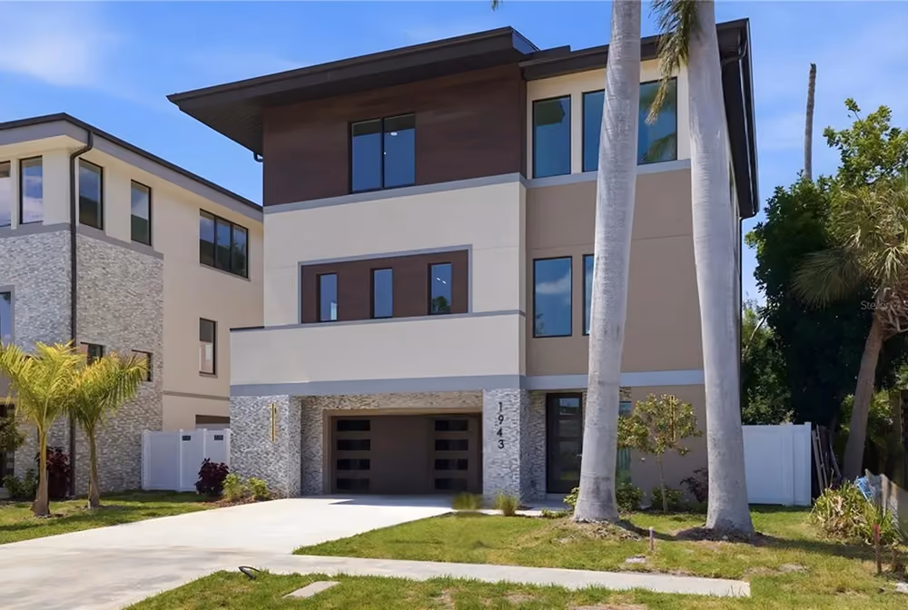 Modern three-story house with stone accents, large windows, driveway, and palm trees in front yard.