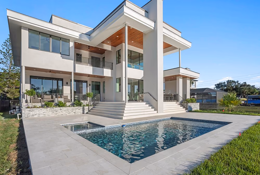 Modern two-story house with large windows, stairs, and a swimming pool in the backyard on a sunny day.