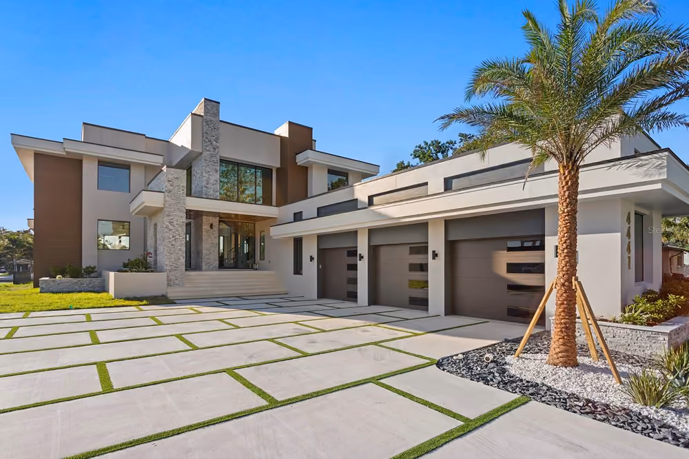 Modern two-story house with stone accents, large windows, a three-car garage, and a palm tree in front yard.
