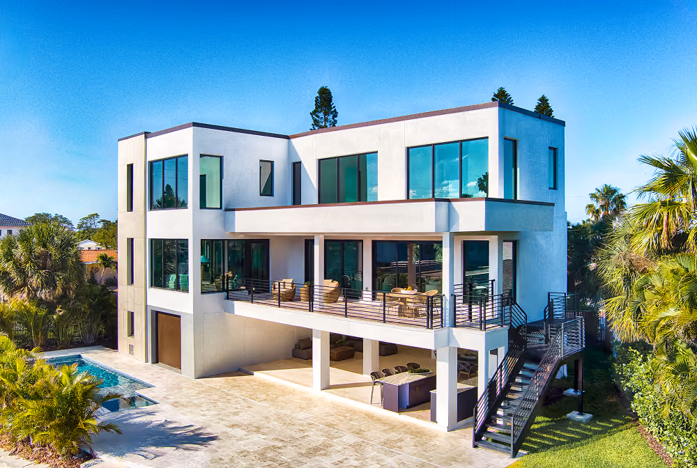 Modern two-story house with large windows, outdoor balcony, pool, and surrounding palm trees.