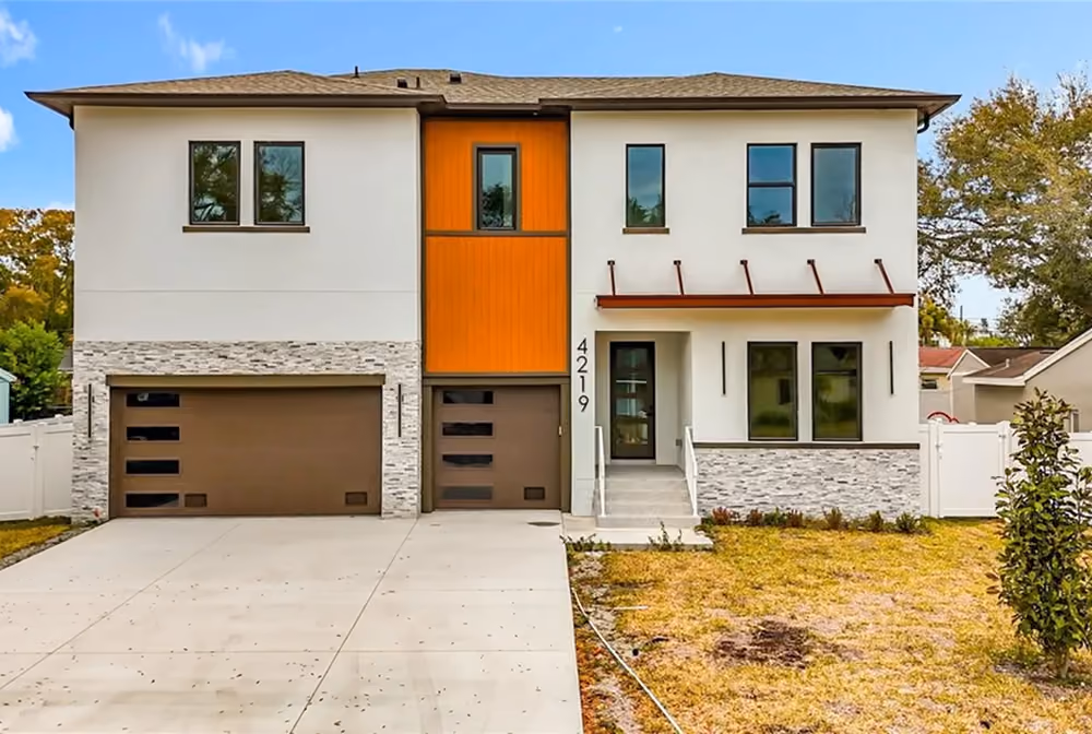 Modern two-story house with white walls, brown garage doors, orange accent, and a concrete driveway.