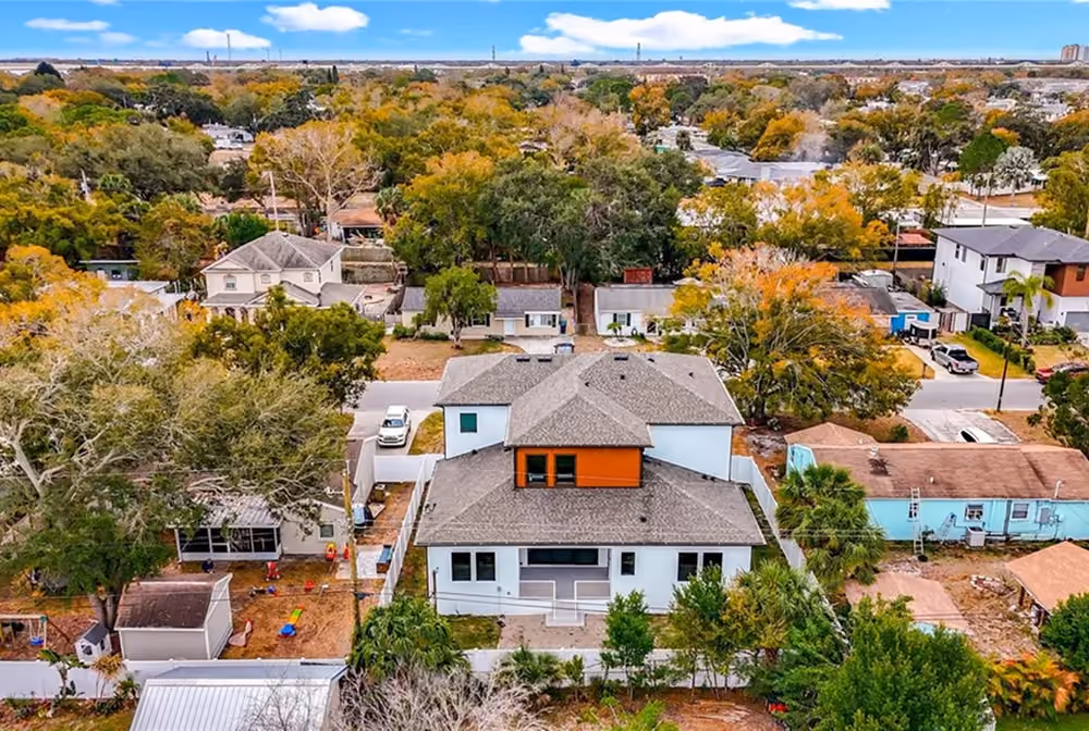 Aerial view of a two-story white house with gray roofs in a neighborhood with colorful trees.