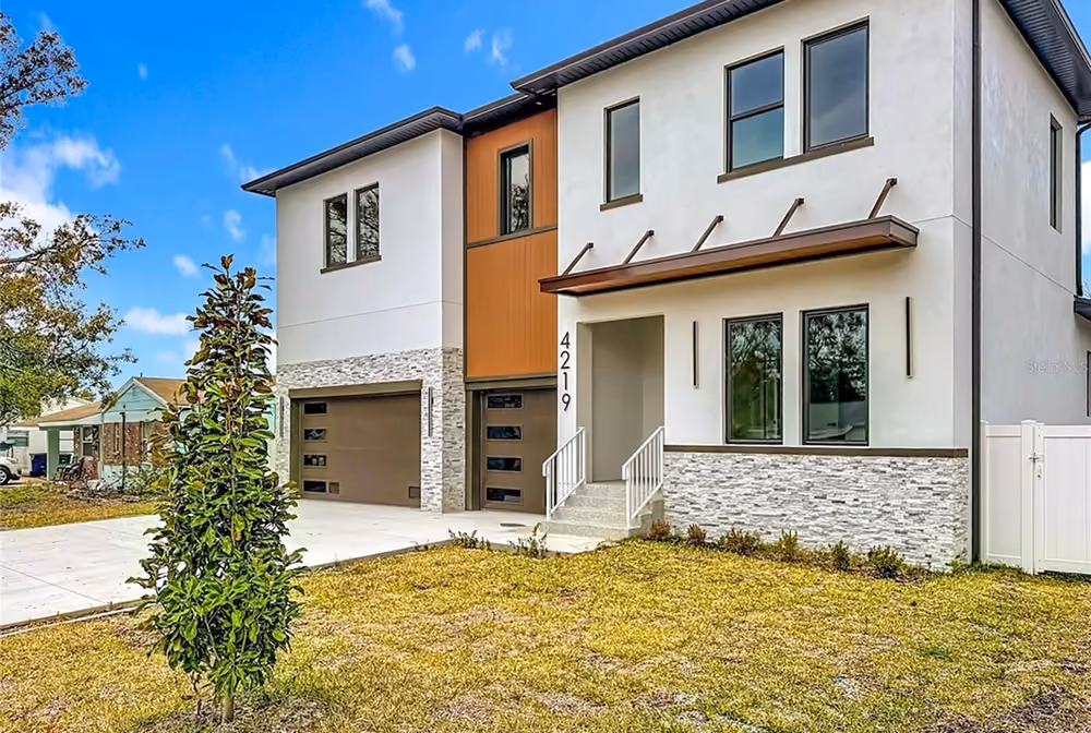 Modern two-story house with stone facade, brown garage doors, and a small front yard with a tree.