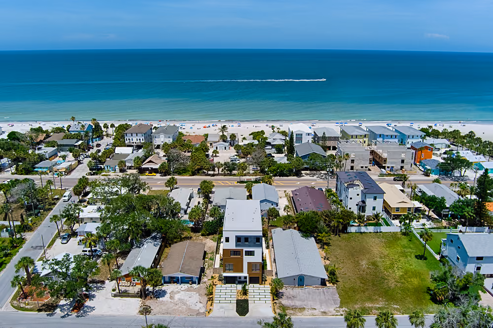 Aerial view of houses near a beach with turquoise ocean water and a boat on the horizon.