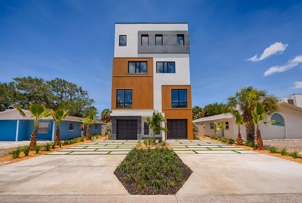 Modern three-story duplex with wood and gray accents, surrounded by palm trees and a clear blue sky.