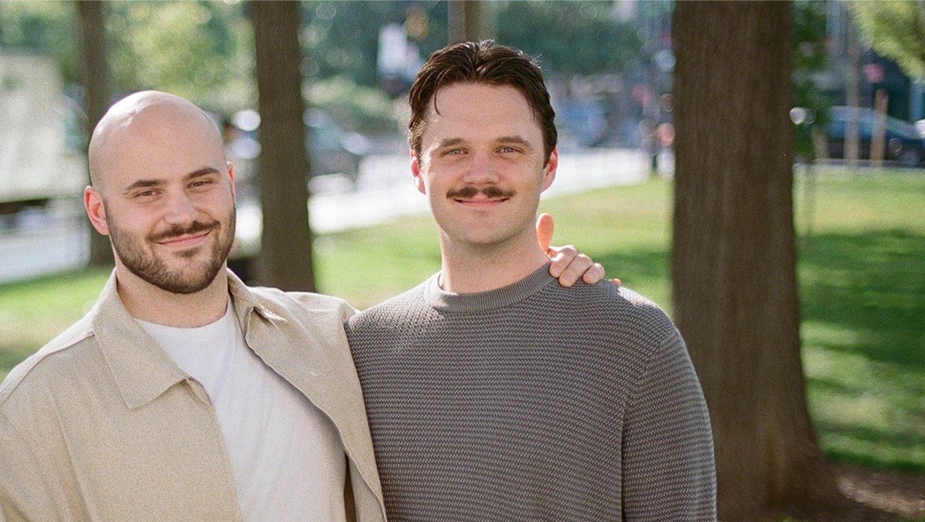 Two casually dressed men leaning against a wooden wall inside a modern building.