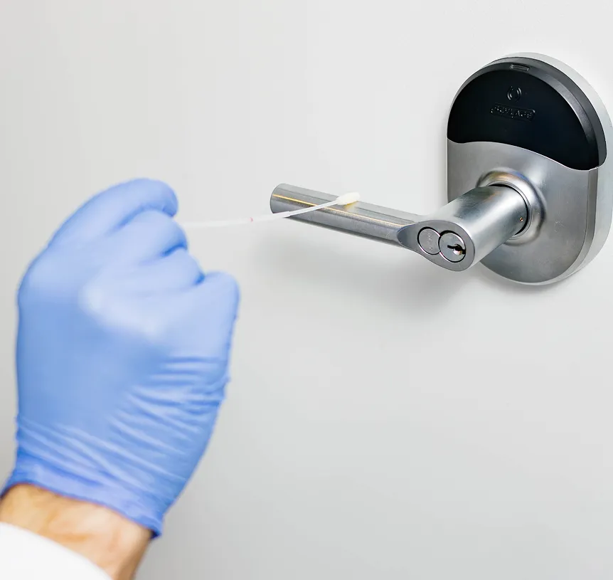 Hand in blue glove swabbing a silver door handle for cleaning or testing.