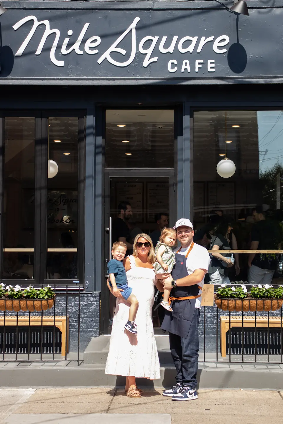 A man, woman and child standing outside of a cafe.