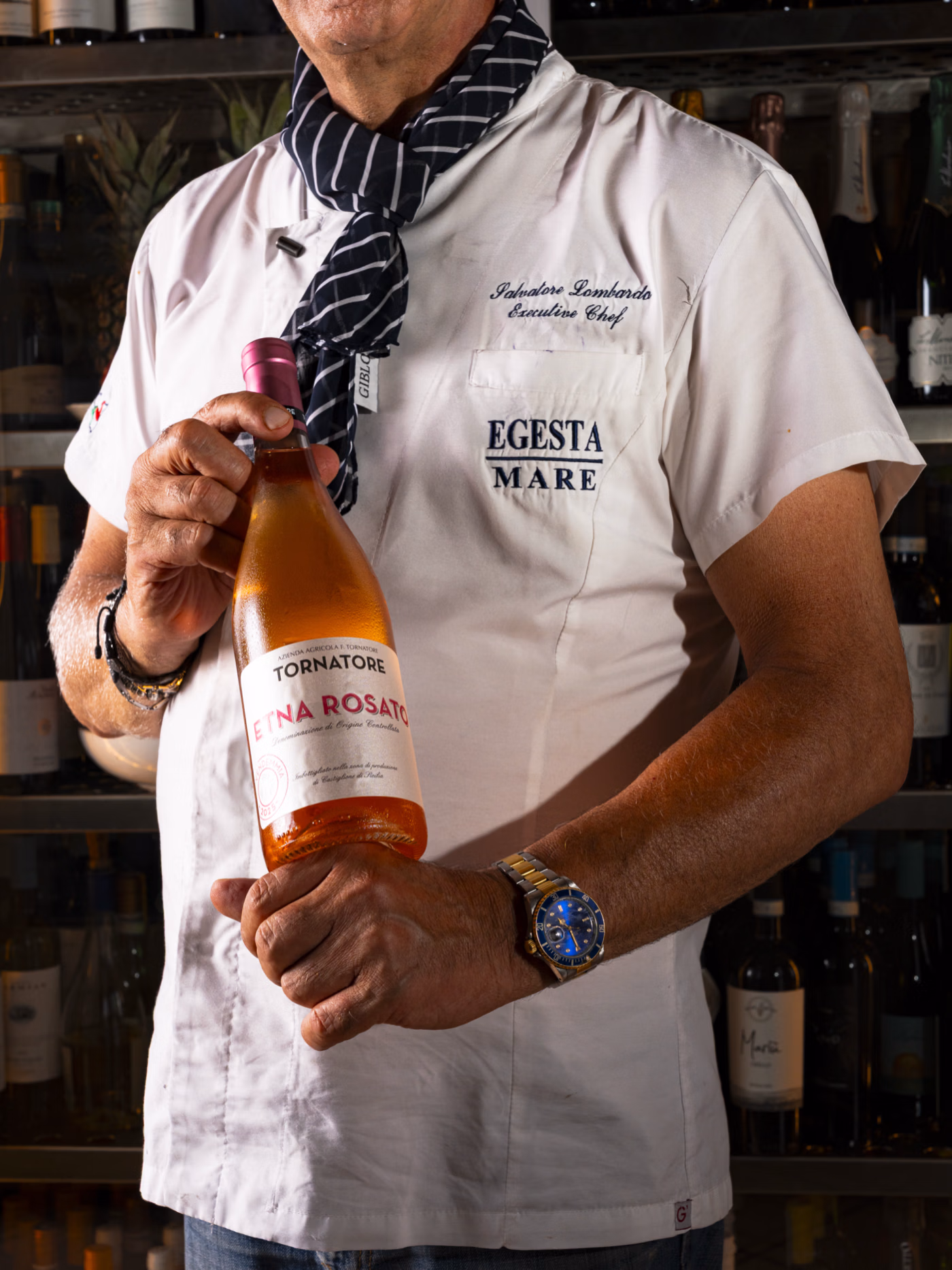 Chef in white uniform holding a bottle of Tornatore Etna Rosato wine.