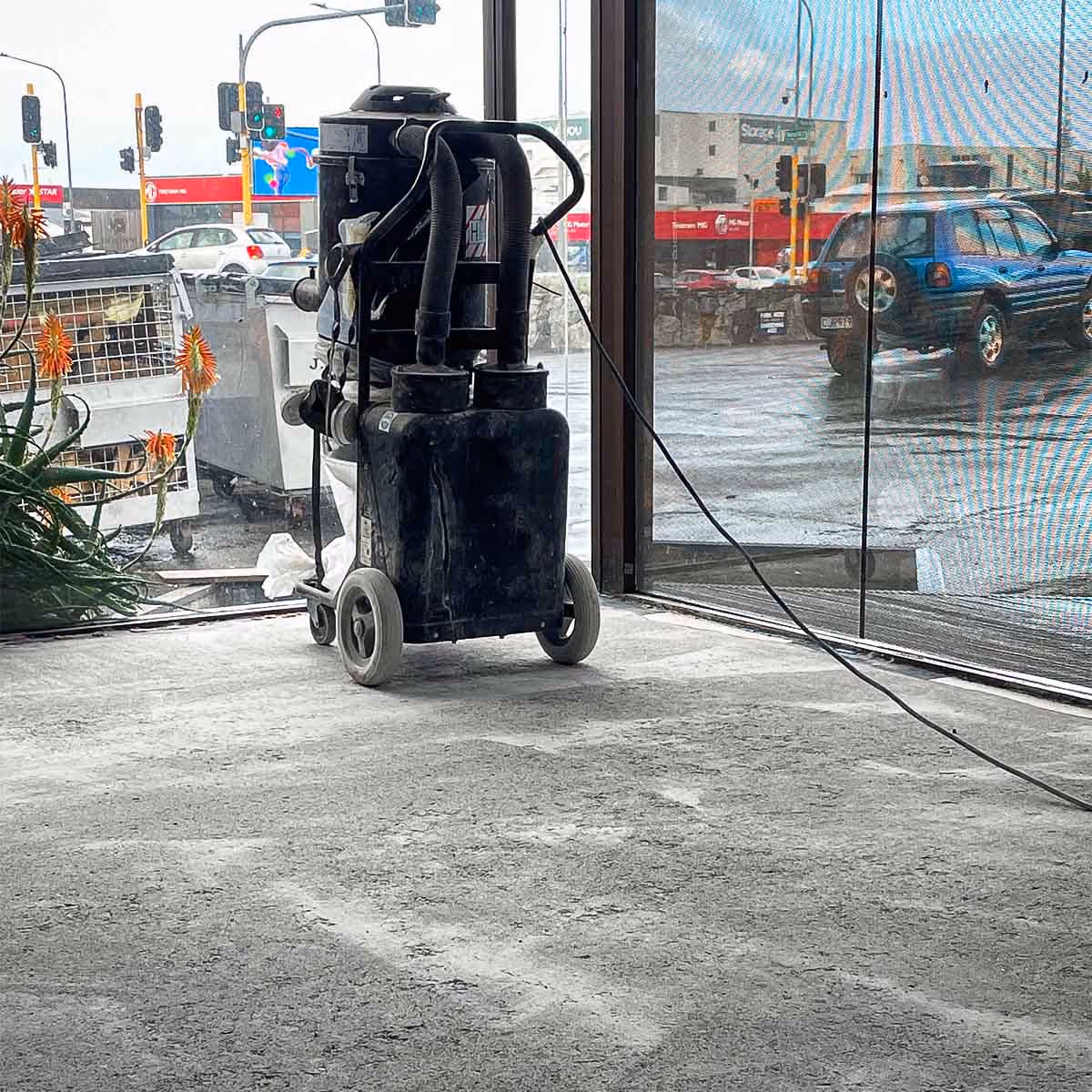 Industrial vacuum or cleaning machine on a cement floor near glass windows overlooking a street and traffic lights.