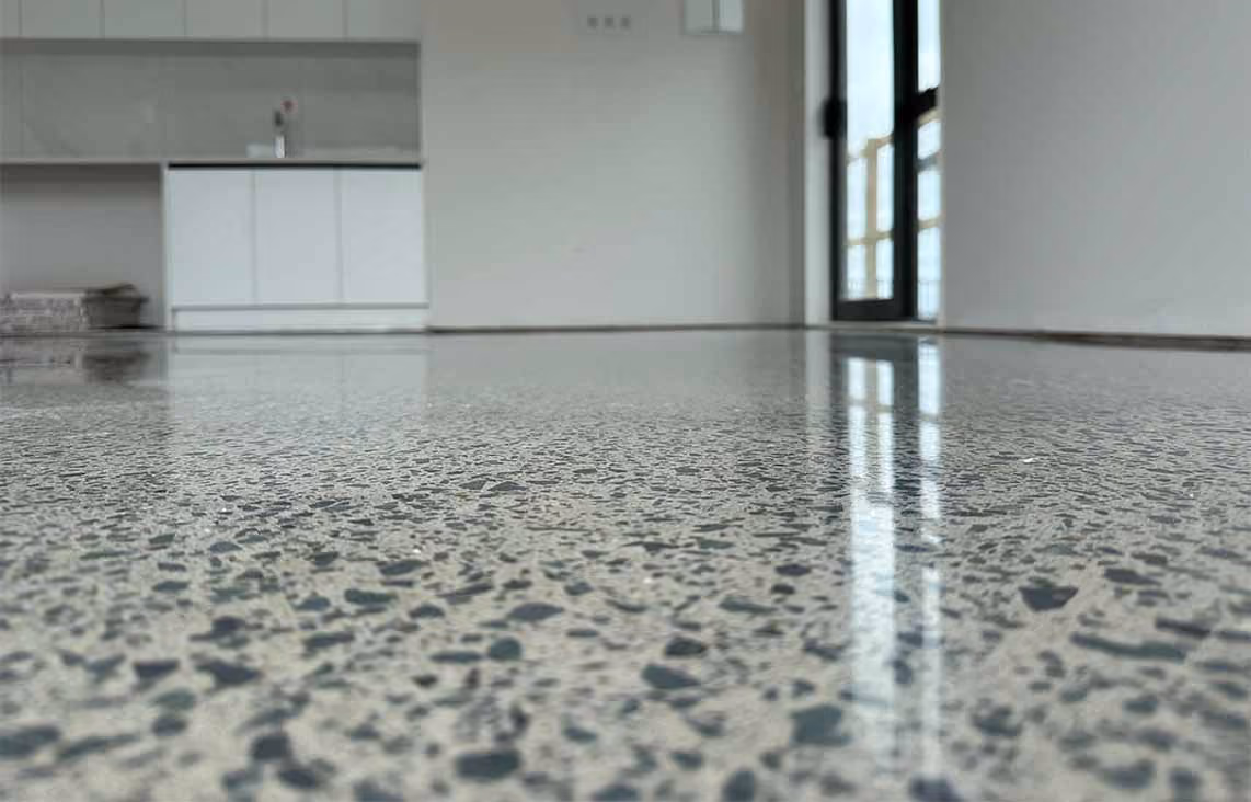 Polished terrazzo floor reflecting light in an empty room with white walls and cabinets.