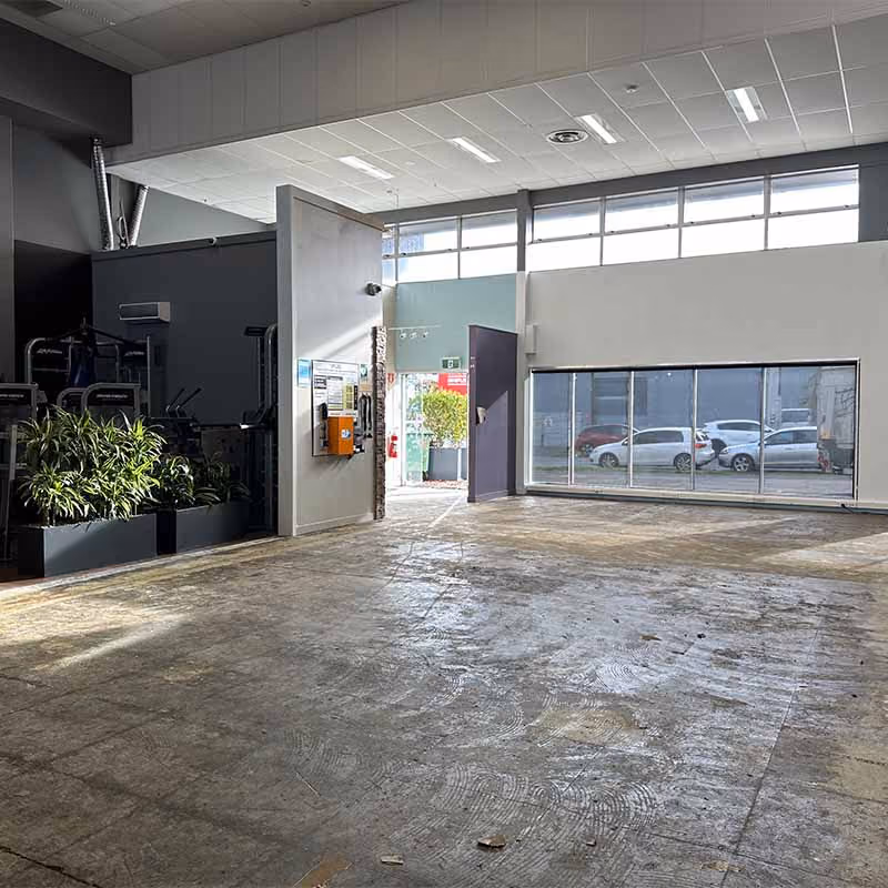 Empty room with concrete floor, large windows showing parked cars outside, and a partially open door.