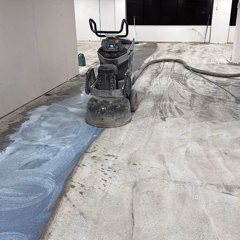 Industrial floor grinder machine polishing concrete floor in an empty room with walls and windows.