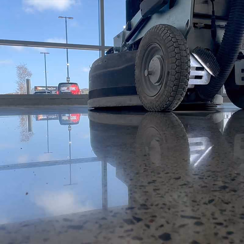 Close-up of a floor polishing machine reflecting on a shiny polished concrete floor inside a building.