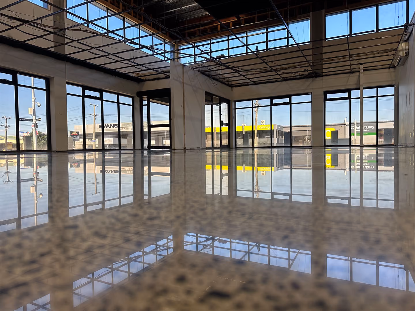 Empty commercial space with large floor-to-ceiling windows and a highly reflective polished floor.