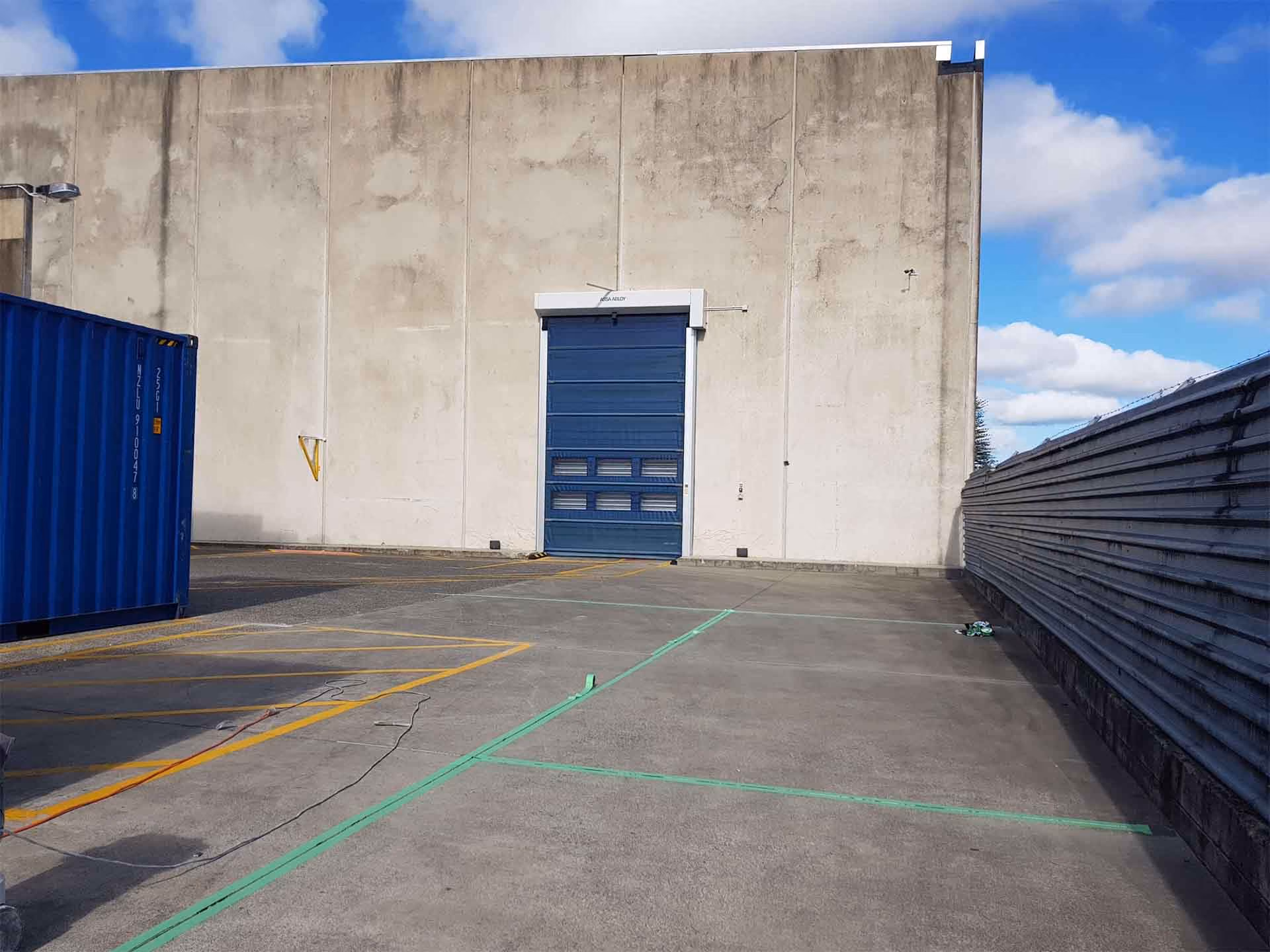 Industrial loading dock with blue closed door, concrete ground marked with green and yellow lines, and shipping container.