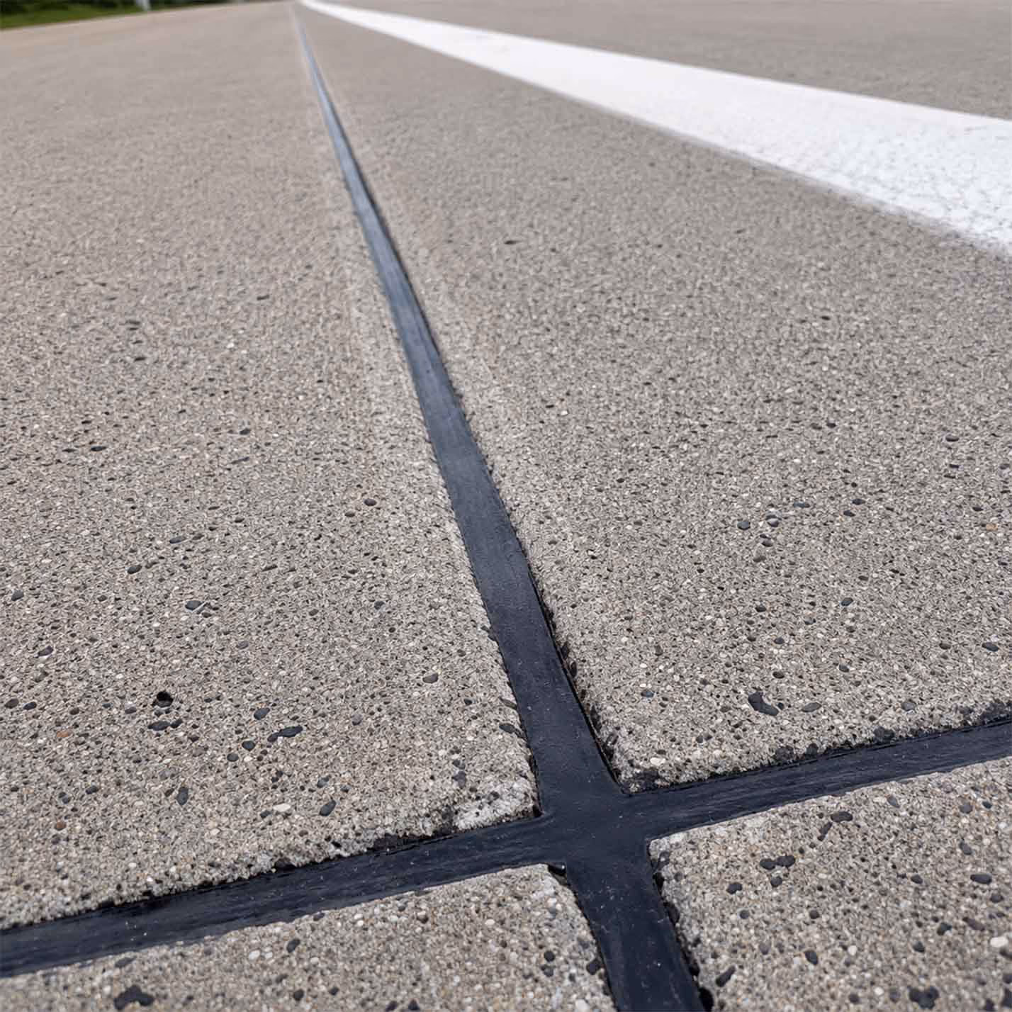 Close-up of black joint sealant filling gaps in concrete pavement with a white painted line nearby.
