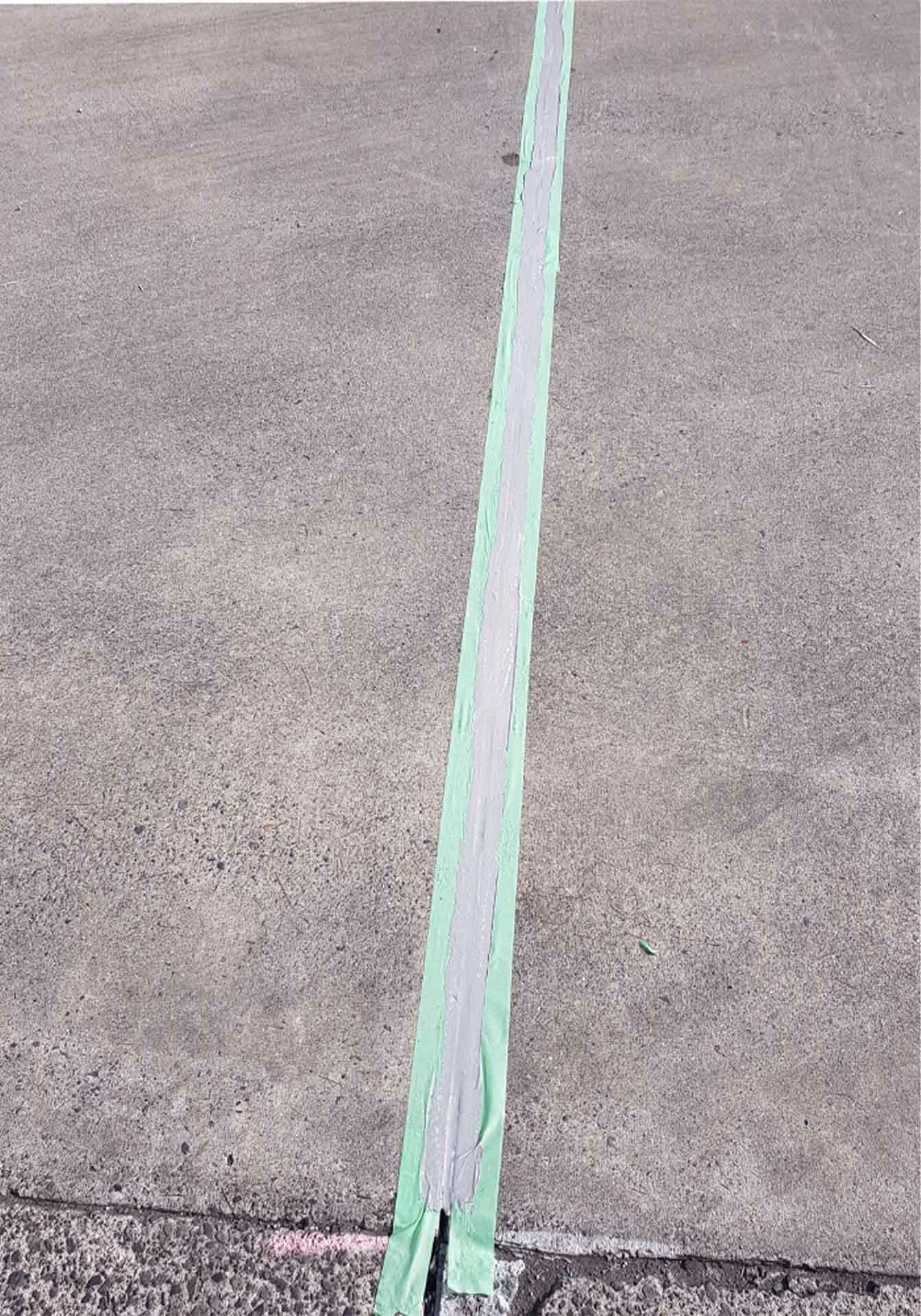 Concrete surface with a seam filled with gray sealant and green tape on both sides.