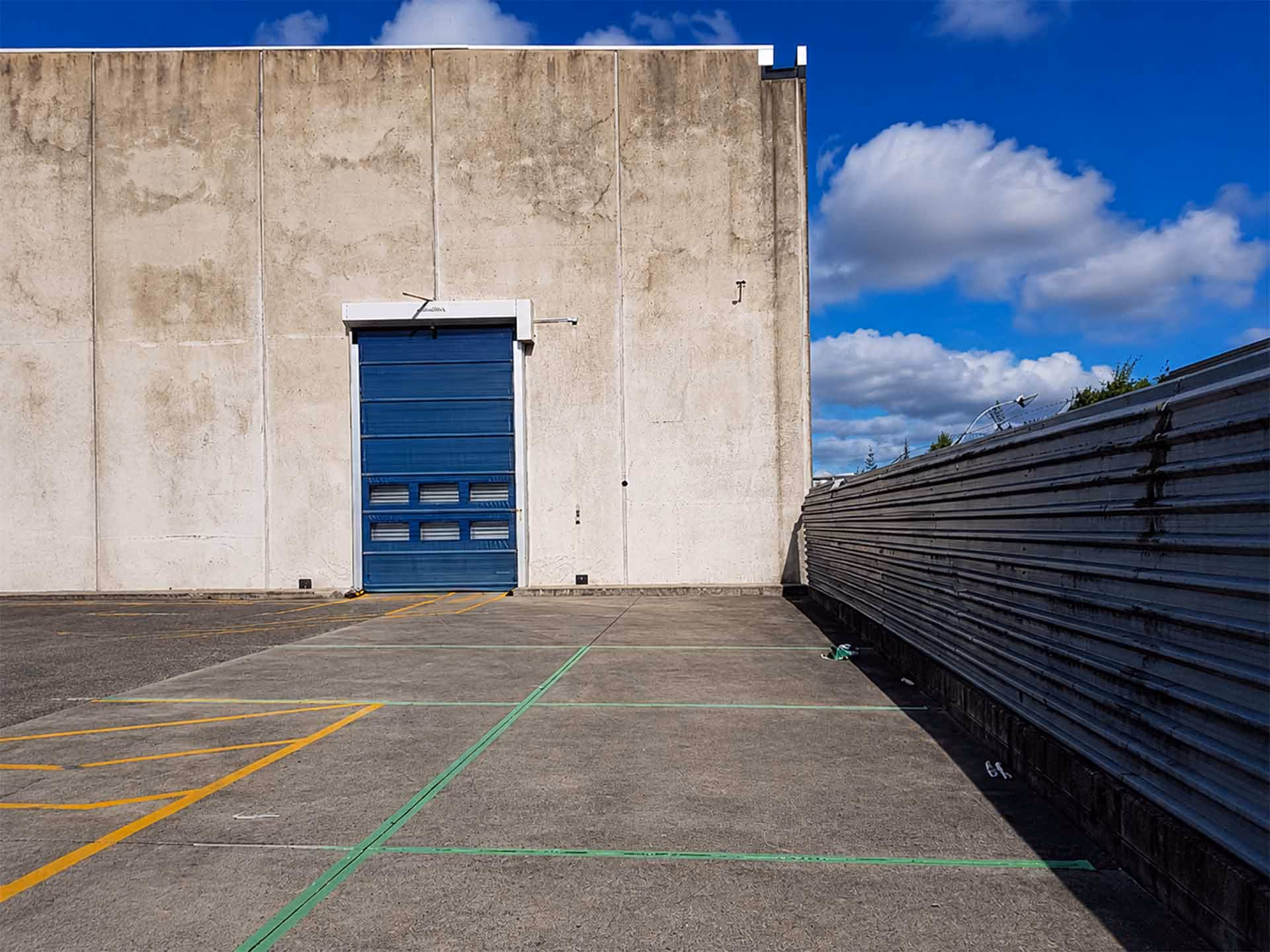 Concrete industrial building with a closed blue garage door under a blue sky with clouds.