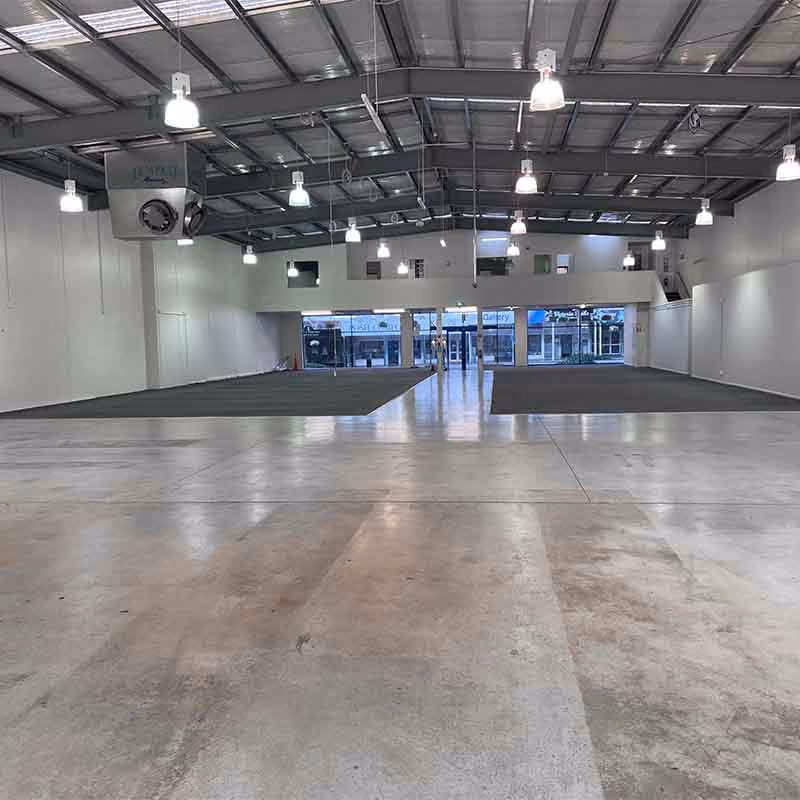 Empty large commercial retail space with polished concrete floor and overhead lights.