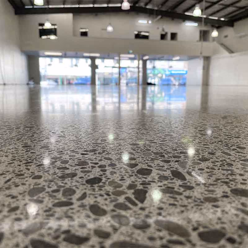 Polished concrete floor in a large, empty commercial warehouse with high ceiling and lights.