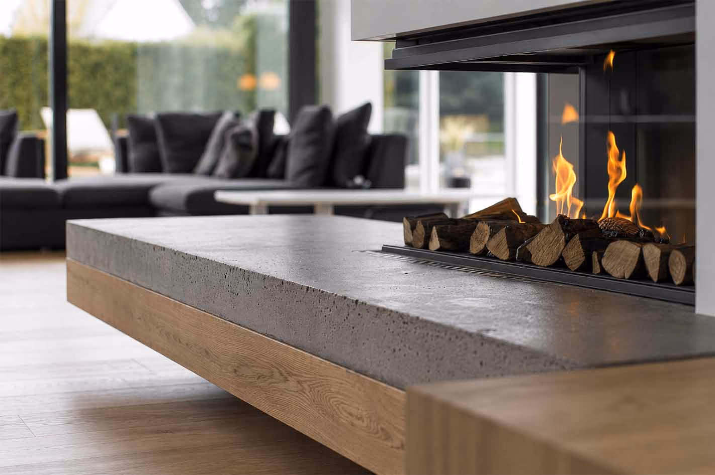 Modern indoor fireplace with burning logs and a concrete and wood hearth in a living room.