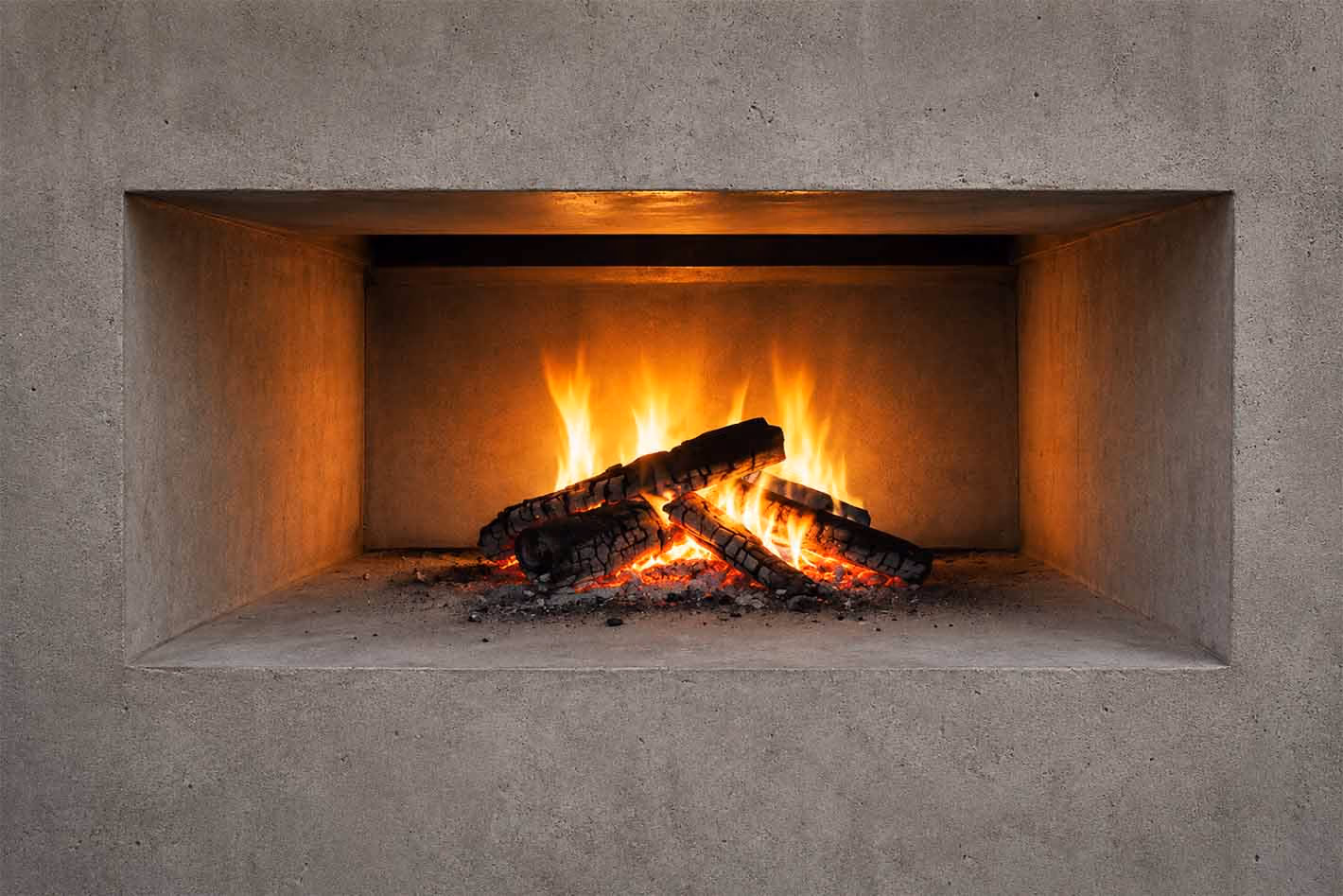 Fire burning with glowing logs inside a rectangular concrete fire pit.