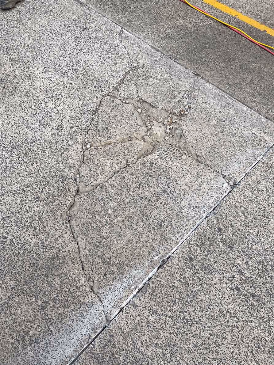 Concrete sidewalk with a large cracked and broken section exposing aggregate beneath.