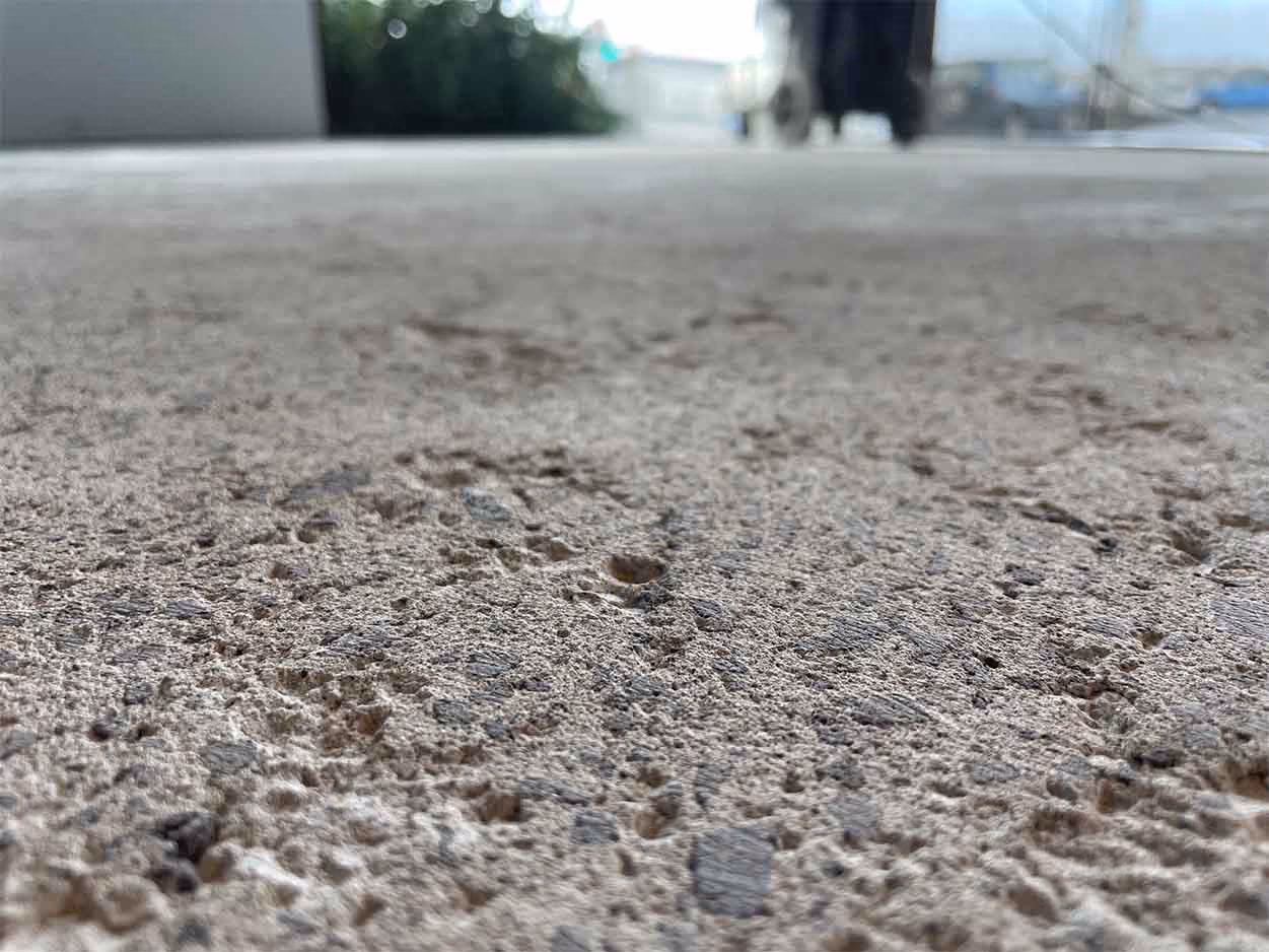 Close-up of textured concrete surface with blurred background objects outdoors.