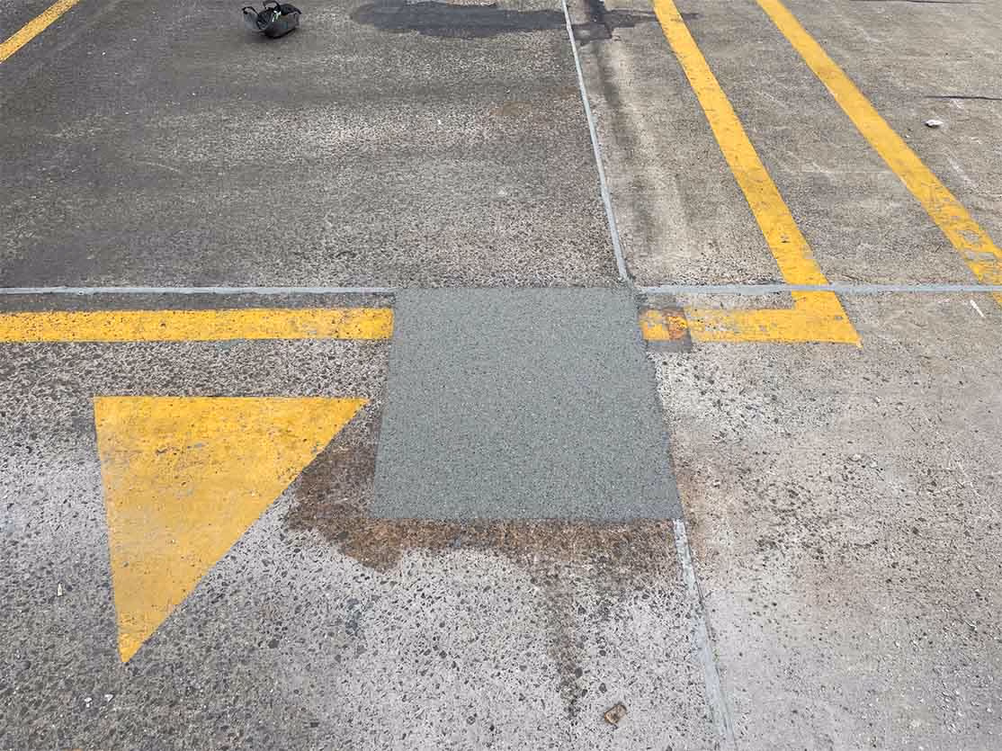 Concrete pavement with fresh square patch repair near faded yellow road markings.