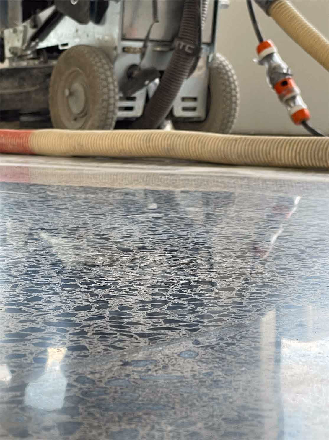 Close-up of polished concrete floor with exposed aggregate and reflection of equipment and hoses.