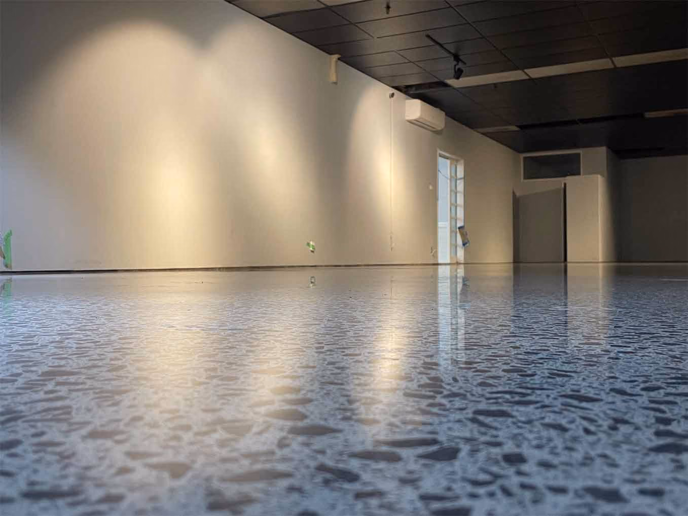 Empty room with polished terrazzo floor, white walls, black ceiling, and air conditioning unit.