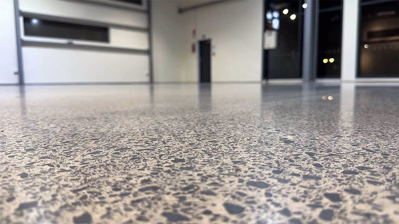 Close-up of polished terrazzo floor in empty room with windows and doors in background.