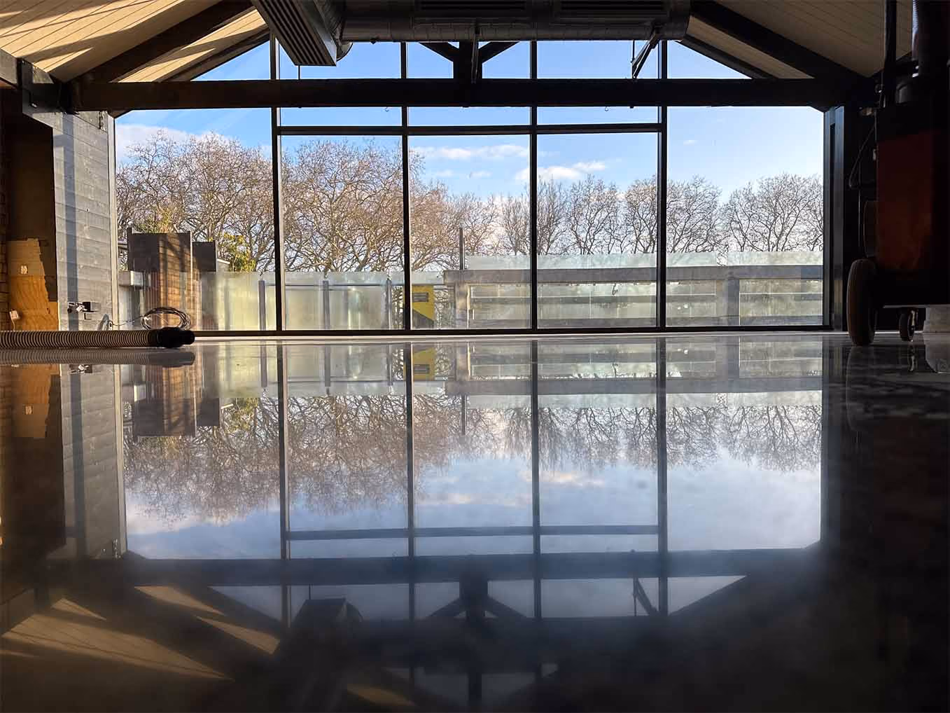Polished concrete floor reflecting a large window with a view of leafless trees outside.