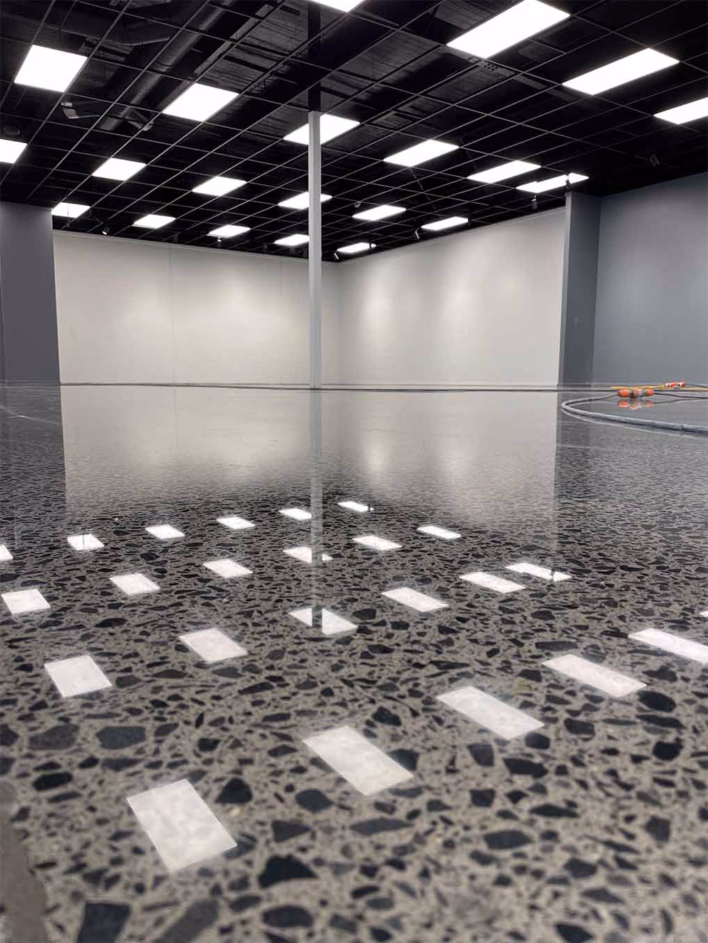Polished terrazzo floor reflecting overhead lights in an empty commercial space with white walls and black ceiling.