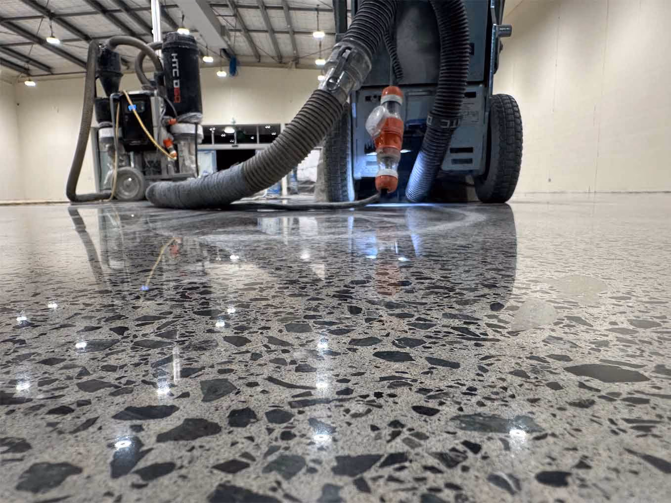 Polished concrete floor with reflection of ceiling lights and floor polishing machines indoors.