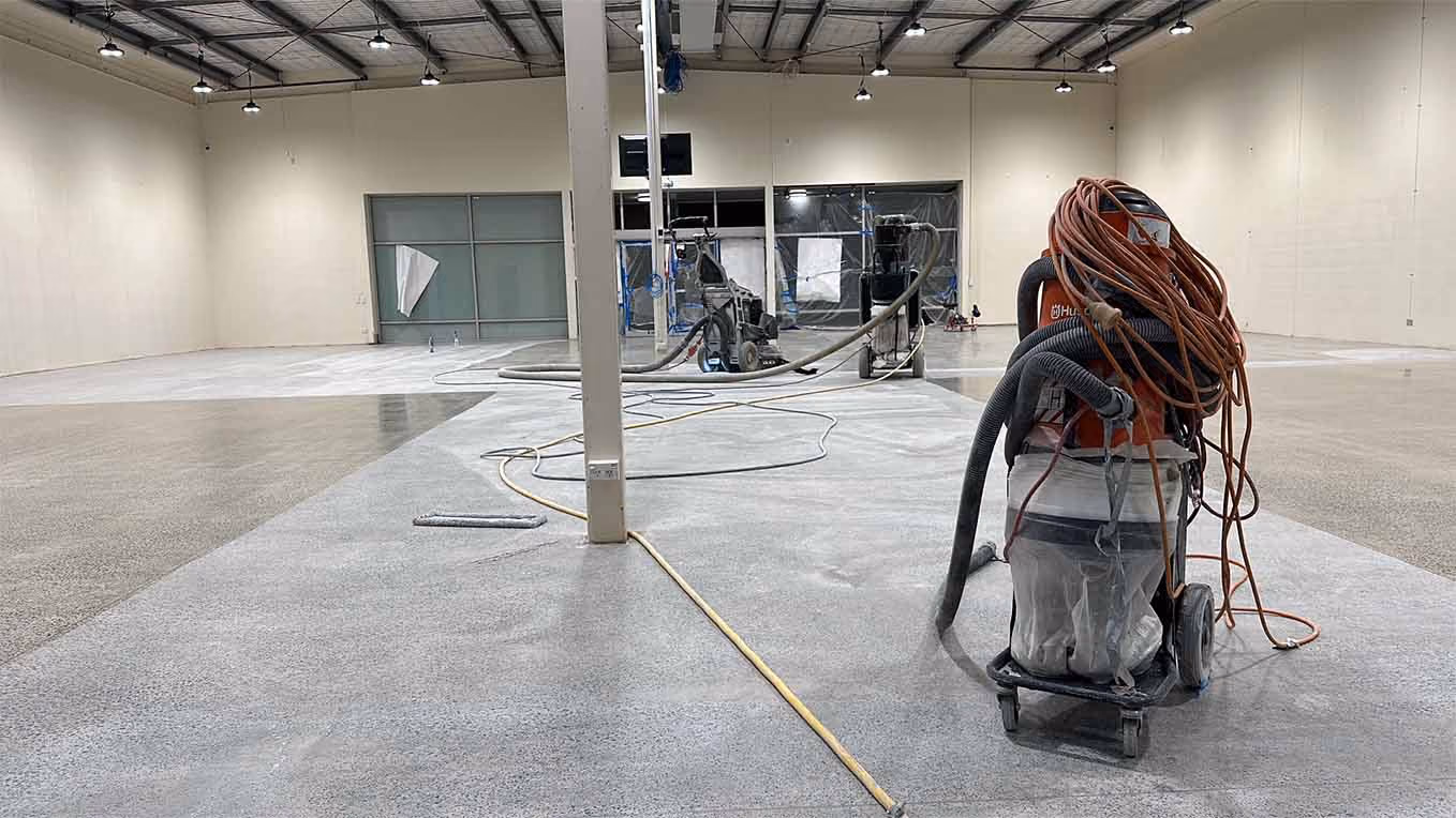 Large industrial space with concrete floor being polished by floor cleaning machines and equipment.