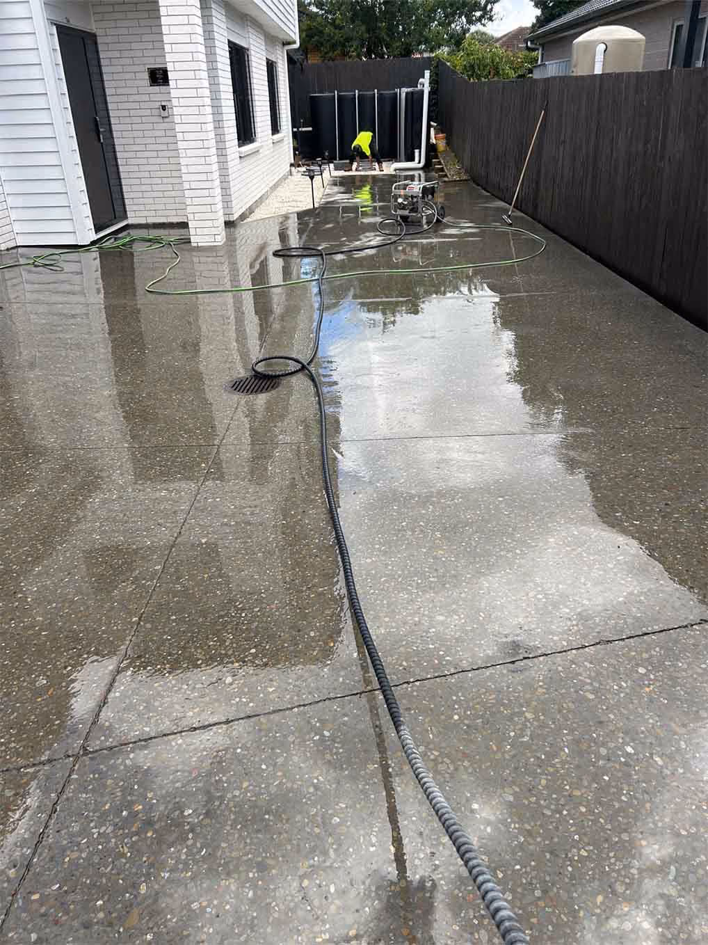 Wet concrete driveway next to white house with a worker in a yellow shirt at the far end.