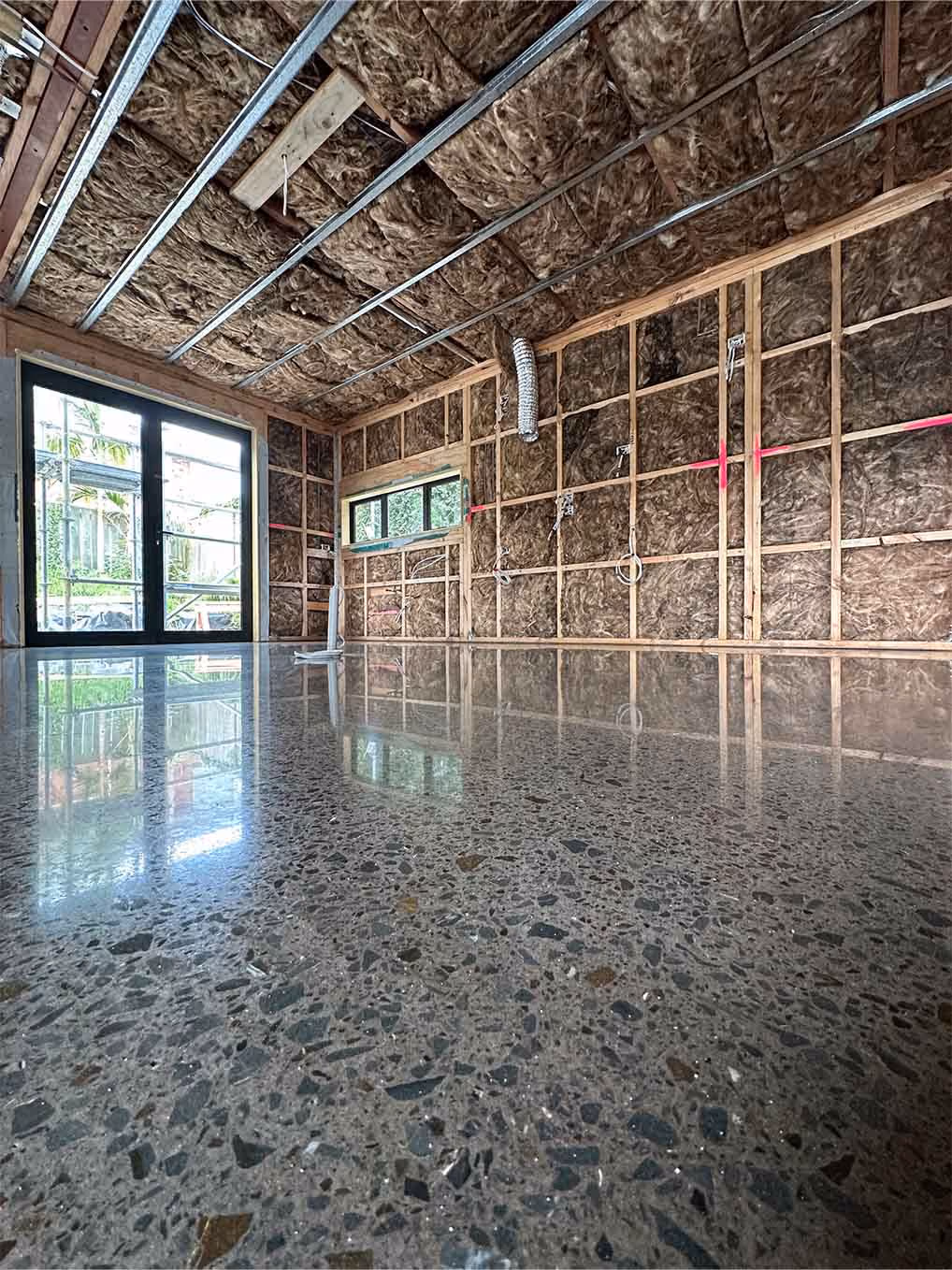 Polished concrete floor in unfinished room with exposed insulation and wooden framing.