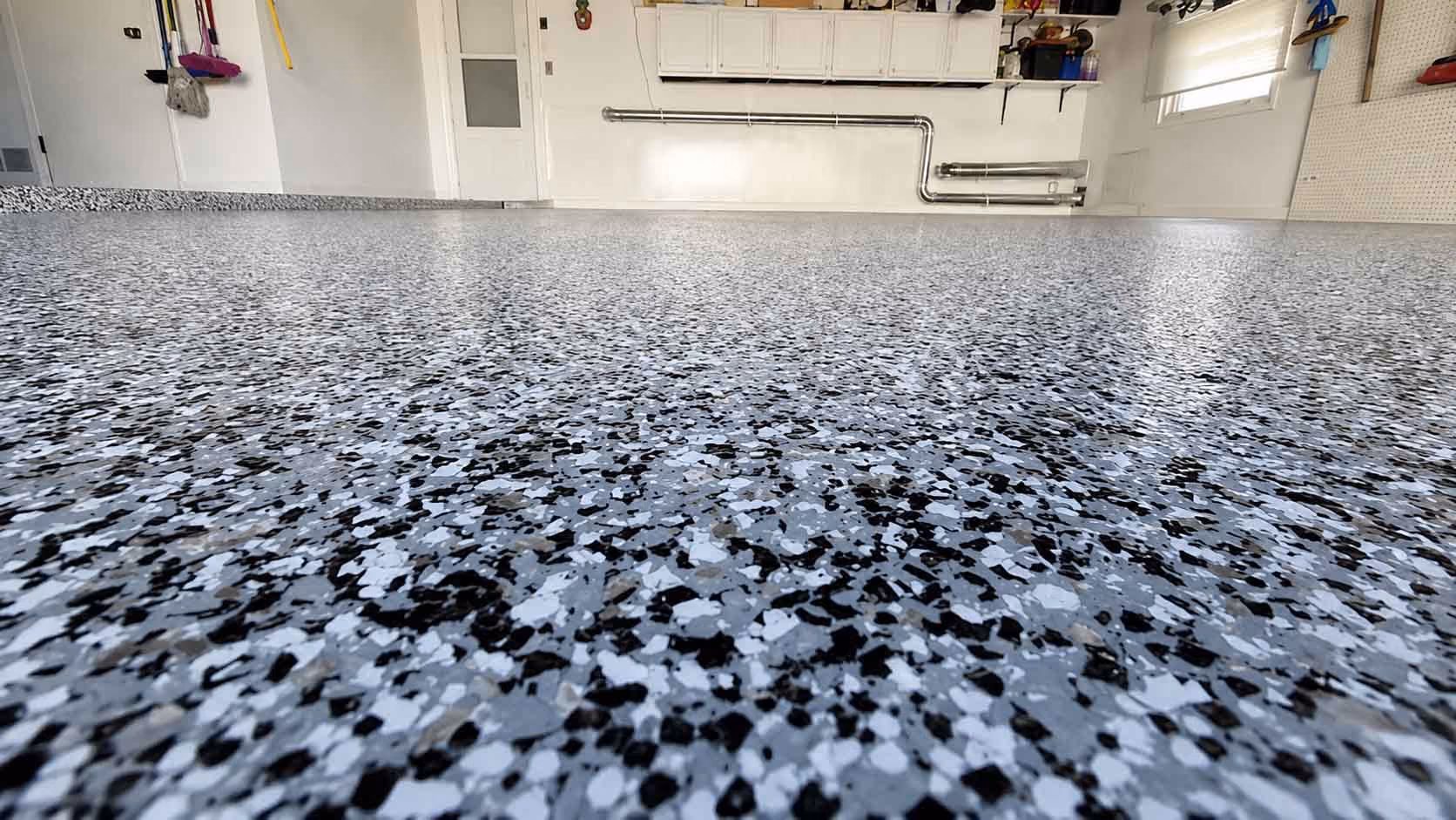 Speckled epoxy garage floor in gray, black, and white with white walls and cabinets.